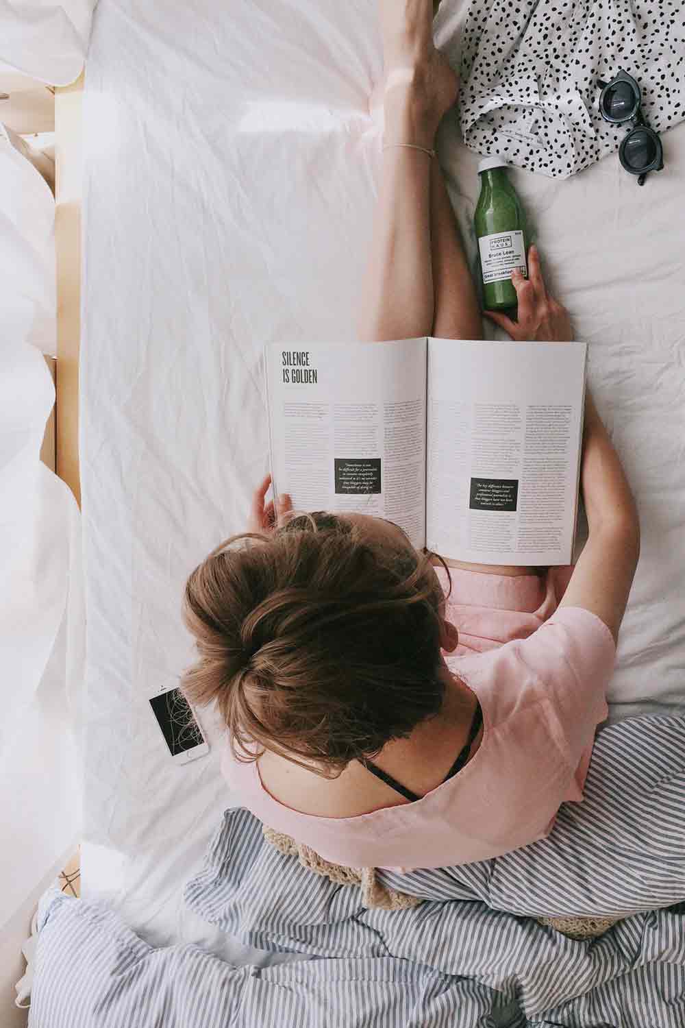 woman-in-pink-dress-sitting-on-bed-while-reading-698158
